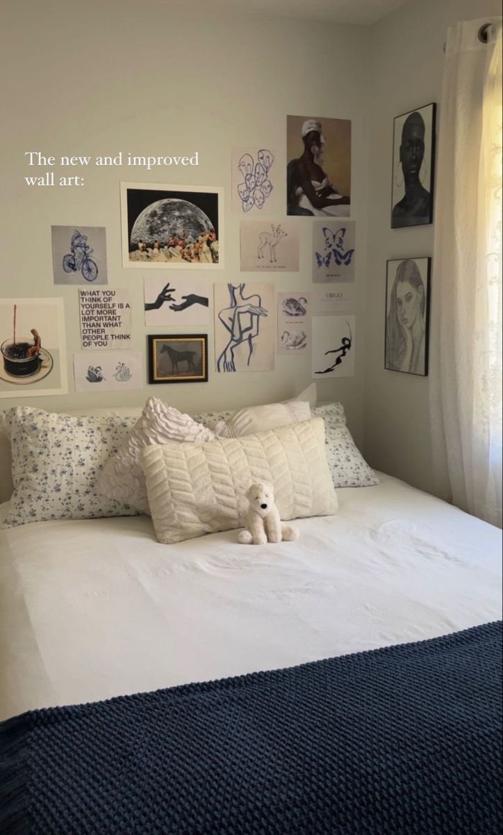 a white bed topped with lots of pillows next to a wall covered in pictures and drawings