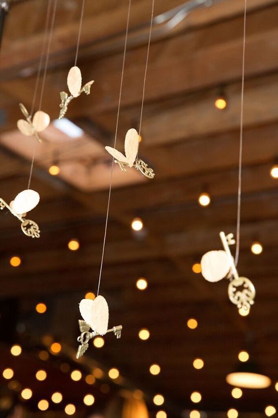 some white paper butterflies hanging from strings in a room with lights on the walls and ceiling