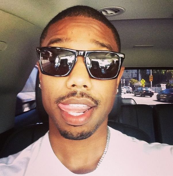 a man wearing sunglasses in the back seat of a car with his tongue hanging out