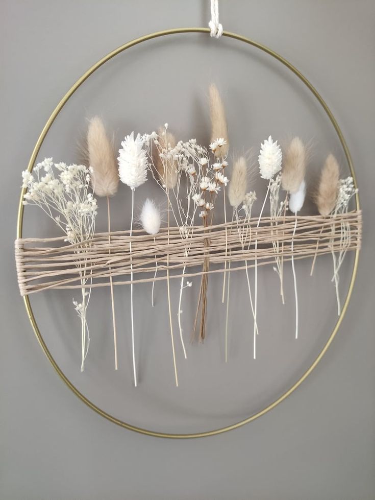 a circular metal frame with dried flowers on it, hanging from the wall in front of a gray wall