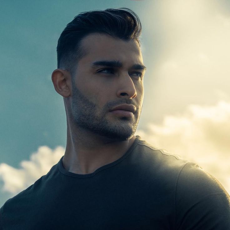 a man standing in front of the sun wearing a black shirt and looking off into the distance