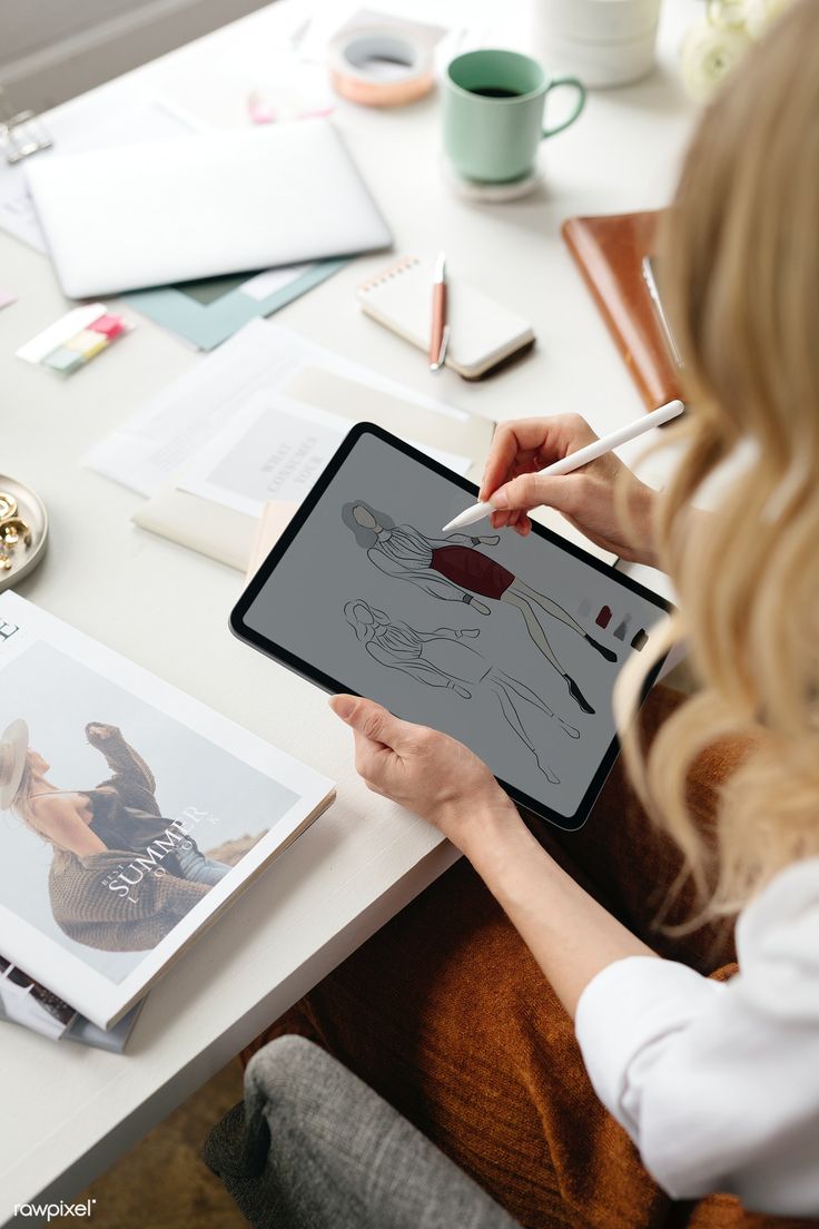 a woman sitting at a table with an ipad and drawing on the screen while holding a pencil in her hand