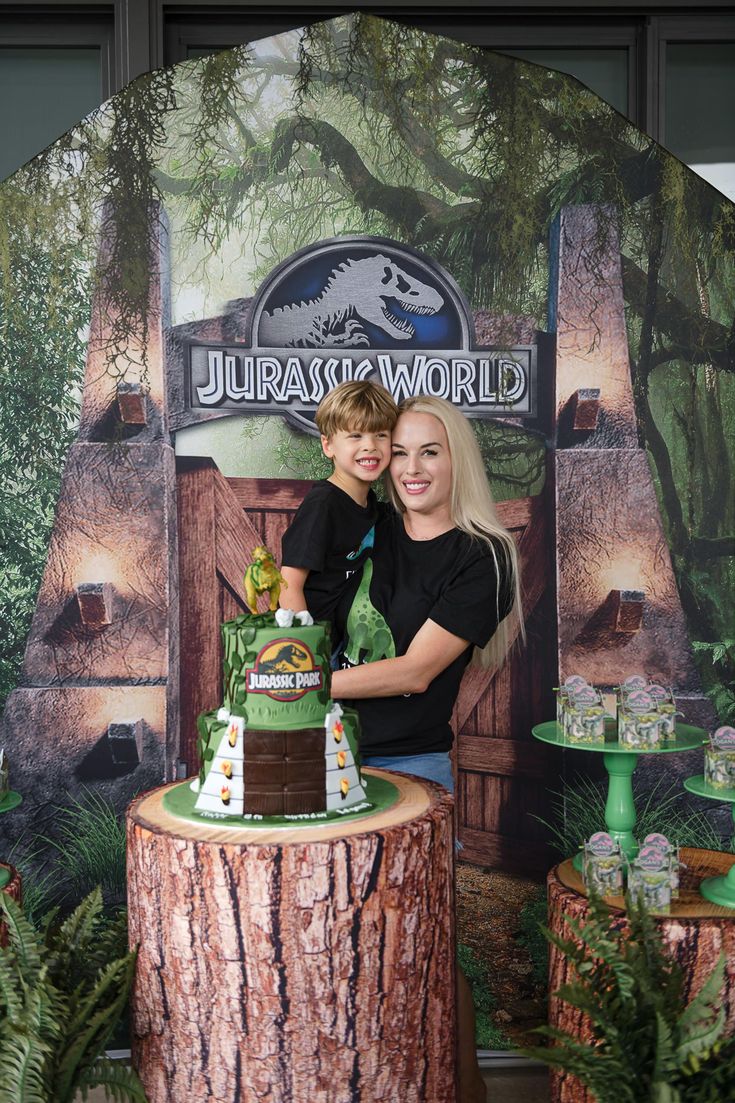 two people standing behind a cake on top of a tree stump in front of a backdrop