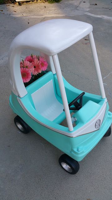 a blue and white toy car with flowers in the passenger seat sitting on concrete pavement