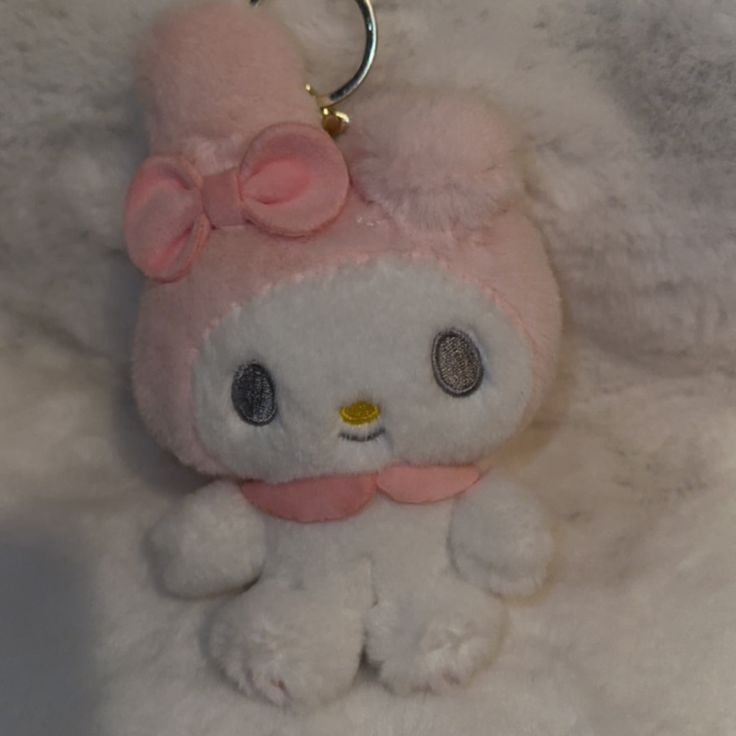 a white stuffed animal with a pink bow on it's head sitting on a furry surface