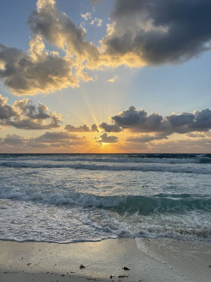 the sun is setting over the ocean with clouds in the sky and waves on the beach