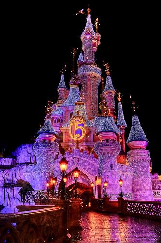the castle is lit up at night with purple lights