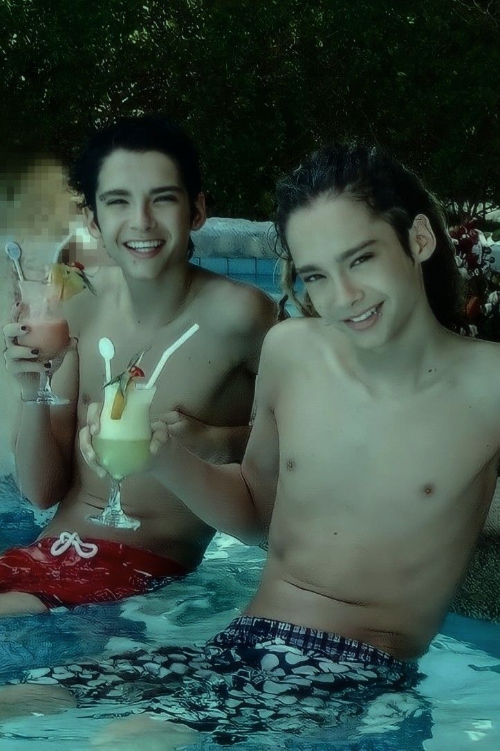 two young men are sitting in the pool drinking cocktails and smiling at the camera