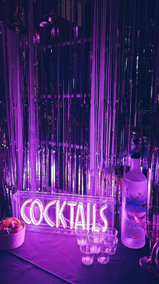 there is a neon sign that says cocktails on the table next to some glasses
