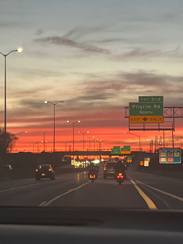 cars driving down the highway at sunset with traffic lights and street signs in the background