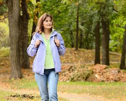 a woman walking down a path in the woods wearing a blue jacket and green shirt