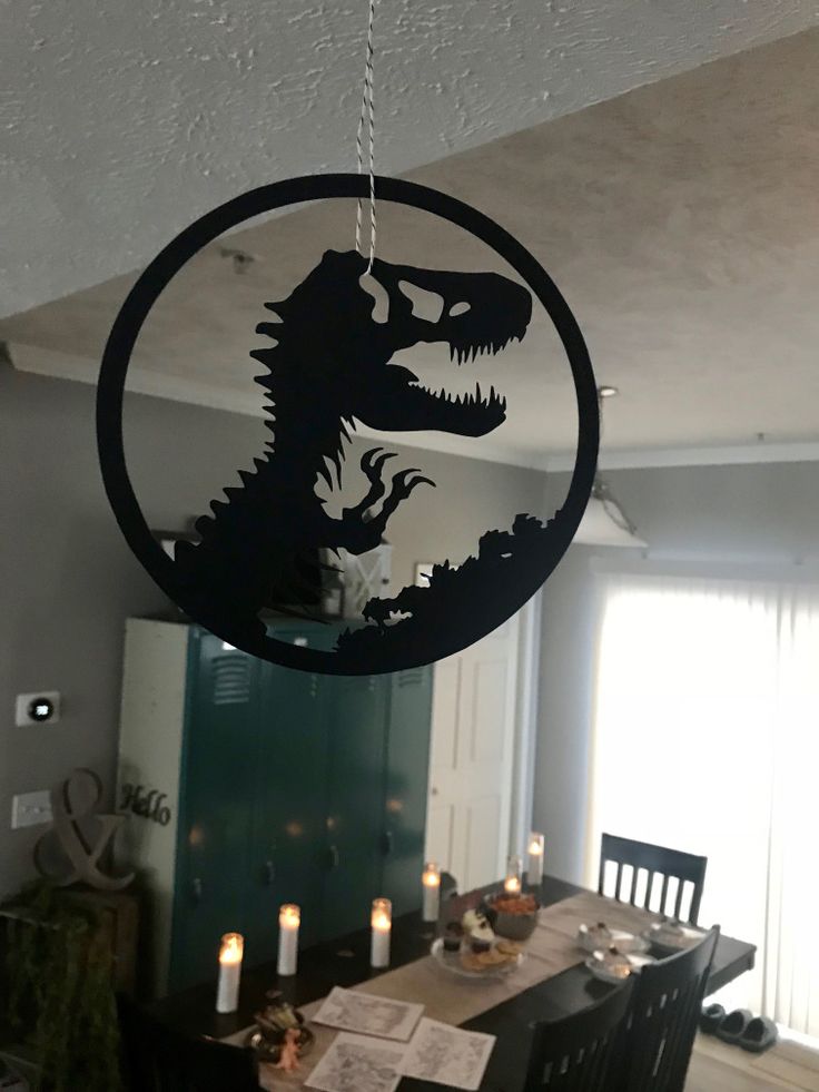 a dining room table with a dinosaur silhouette hanging from it's centerpiece, surrounded by candles