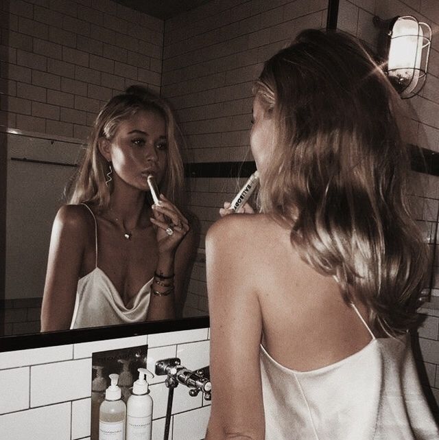 a woman brushing her teeth in front of a bathroom mirror while looking at herself in the mirror