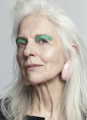 an older woman with long white hair and green eyeliners on her face, looking at the camera