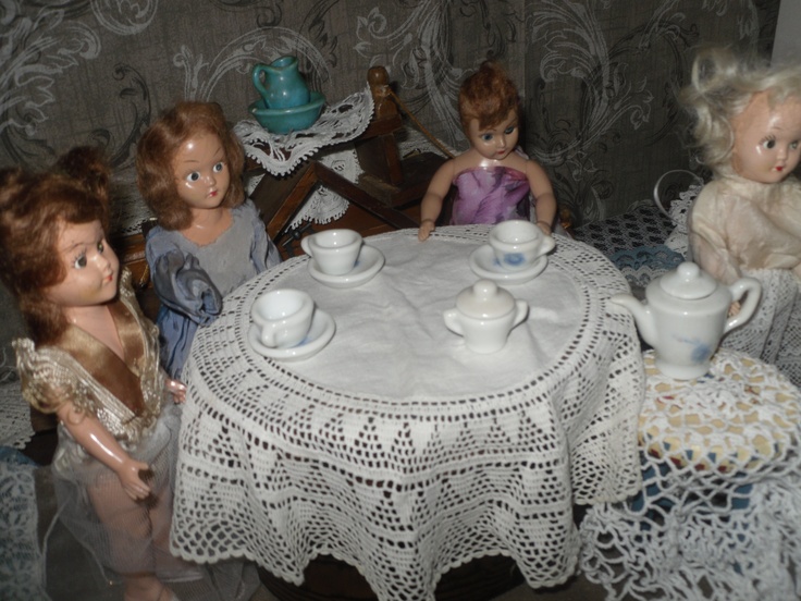 several dolls sitting around a table with tea cups and saucers