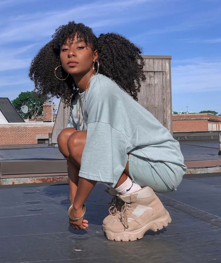 a woman squatting on the ground with her legs crossed, wearing boots and a sweatshirt