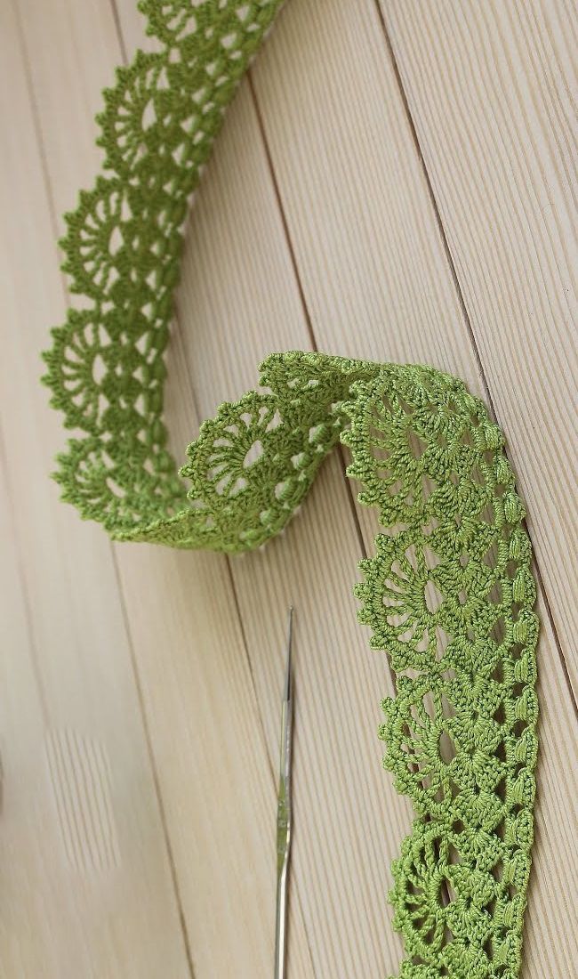 a pair of scissors next to a green crochet doily on a wooden surface