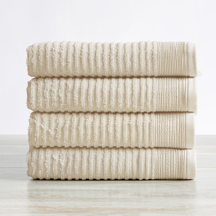 three white towels stacked on top of each other in front of a white wall and floor