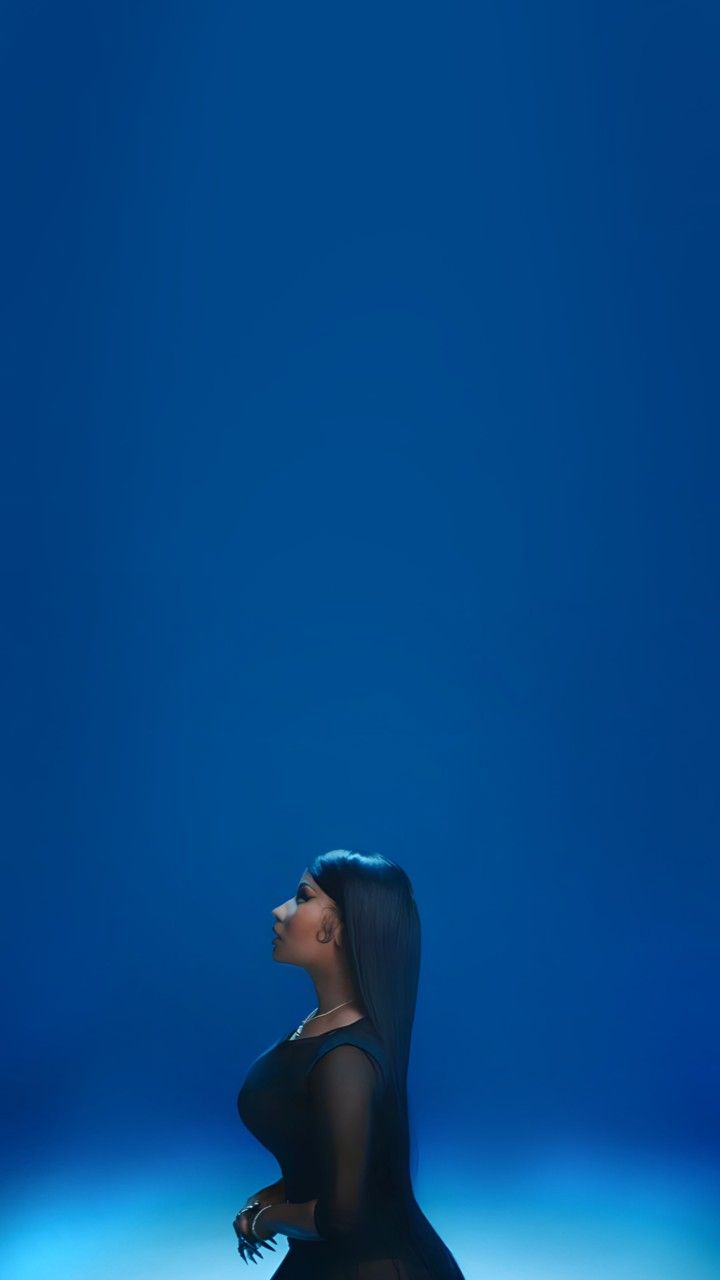 a woman with long black hair sitting on the ground in front of a blue background