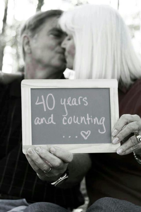 a man and woman kissing each other while holding a chalkboard with the words 40 years and counting written on it