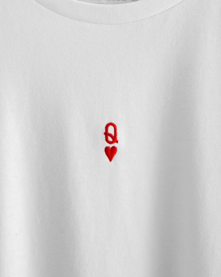 a white t - shirt with a red heart embroidered on the chest and an q in the middle