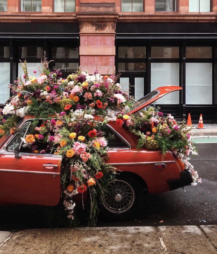 an orange car with flowers on the hood is parked in front of a tall building