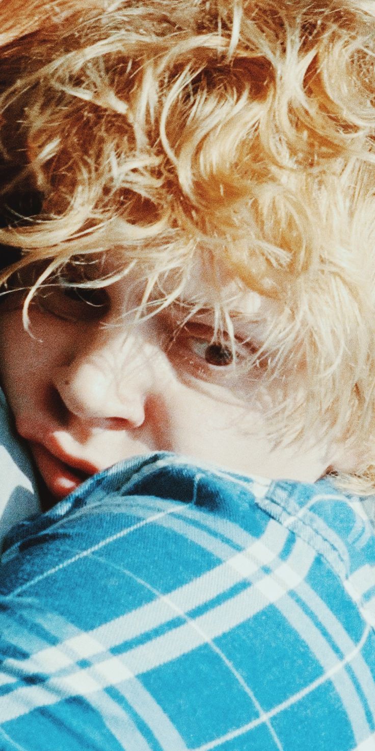 a young boy with curly hair laying on top of a bed next to a pillow