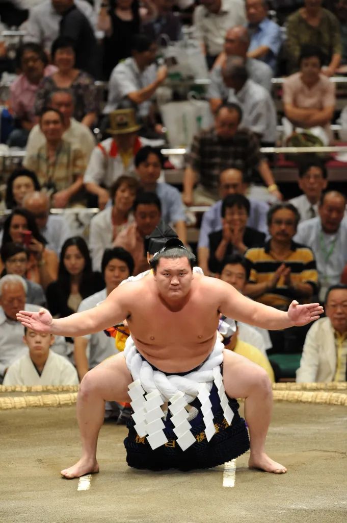 sumo wrestler kneeling on the ground in front of an audience