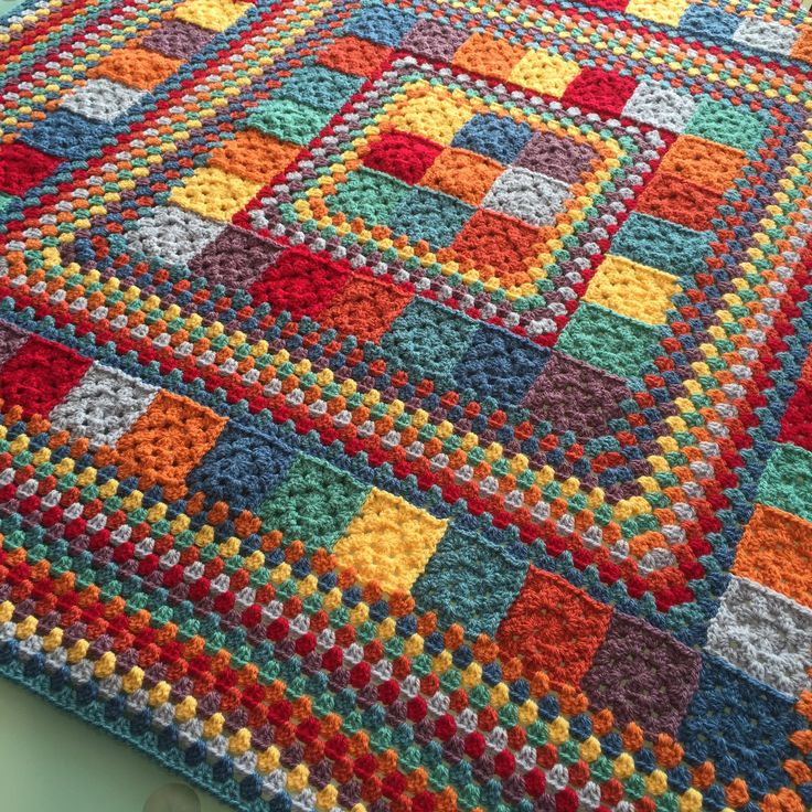 a multicolored crocheted blanket is laying on the floor