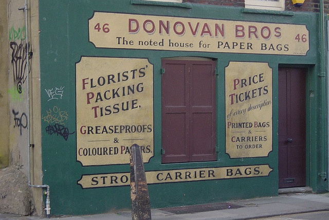 an old building that has been painted green and yellow with advertisements on the front door