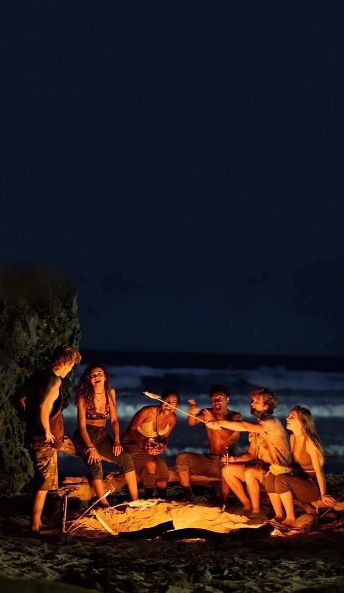 a group of people sitting around a campfire on the beach