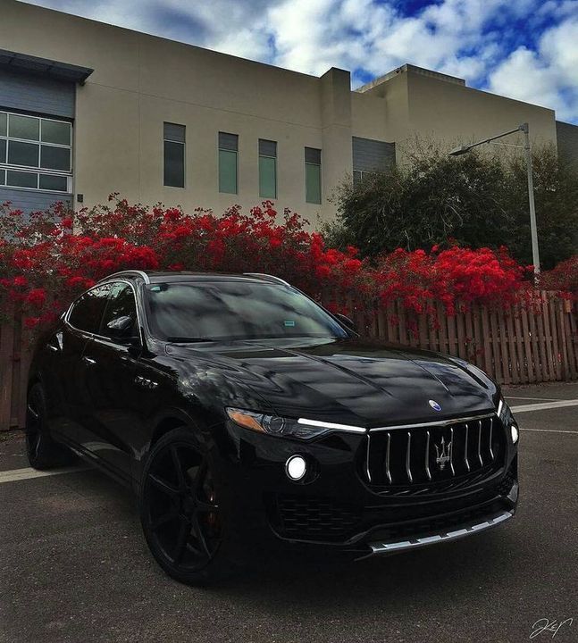 a black masera parked in front of a building with red flowers on the side