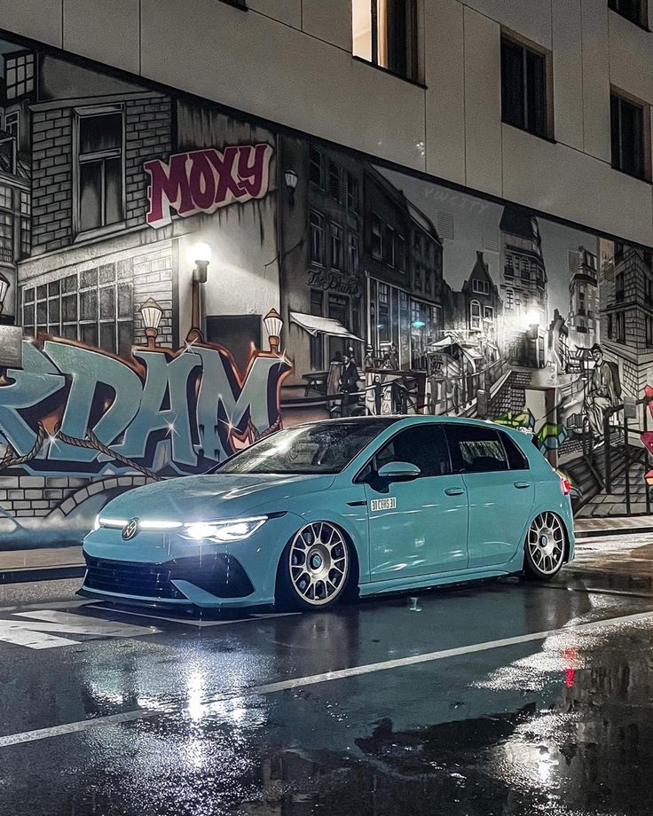 a blue car parked in front of a graffiti covered building on a wet street at night