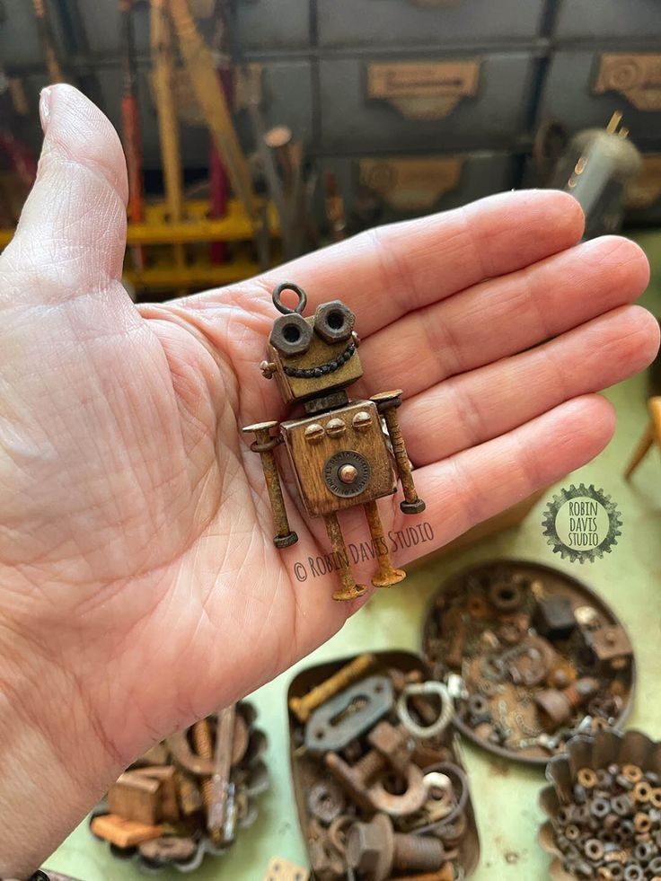 a person's hand holding an old fashioned robot ring in front of many other mechanical parts