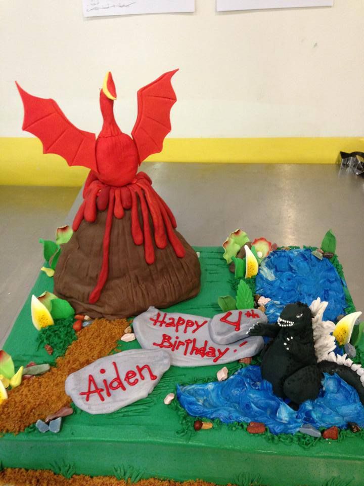 a birthday cake made to look like a volcano and a dragon sitting on the ground