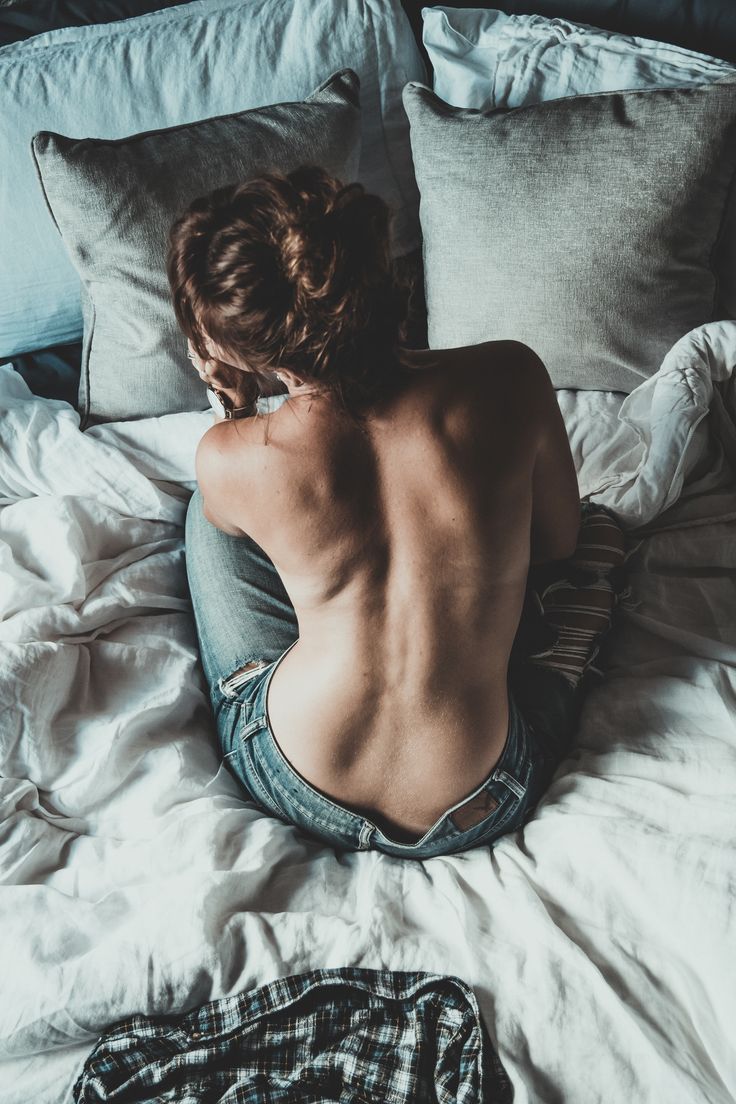 a naked woman sitting on top of a bed next to pillows and blankets with her back turned