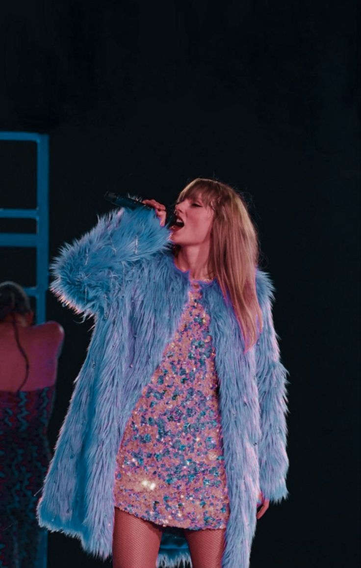 a woman in a blue fur coat singing into a microphone