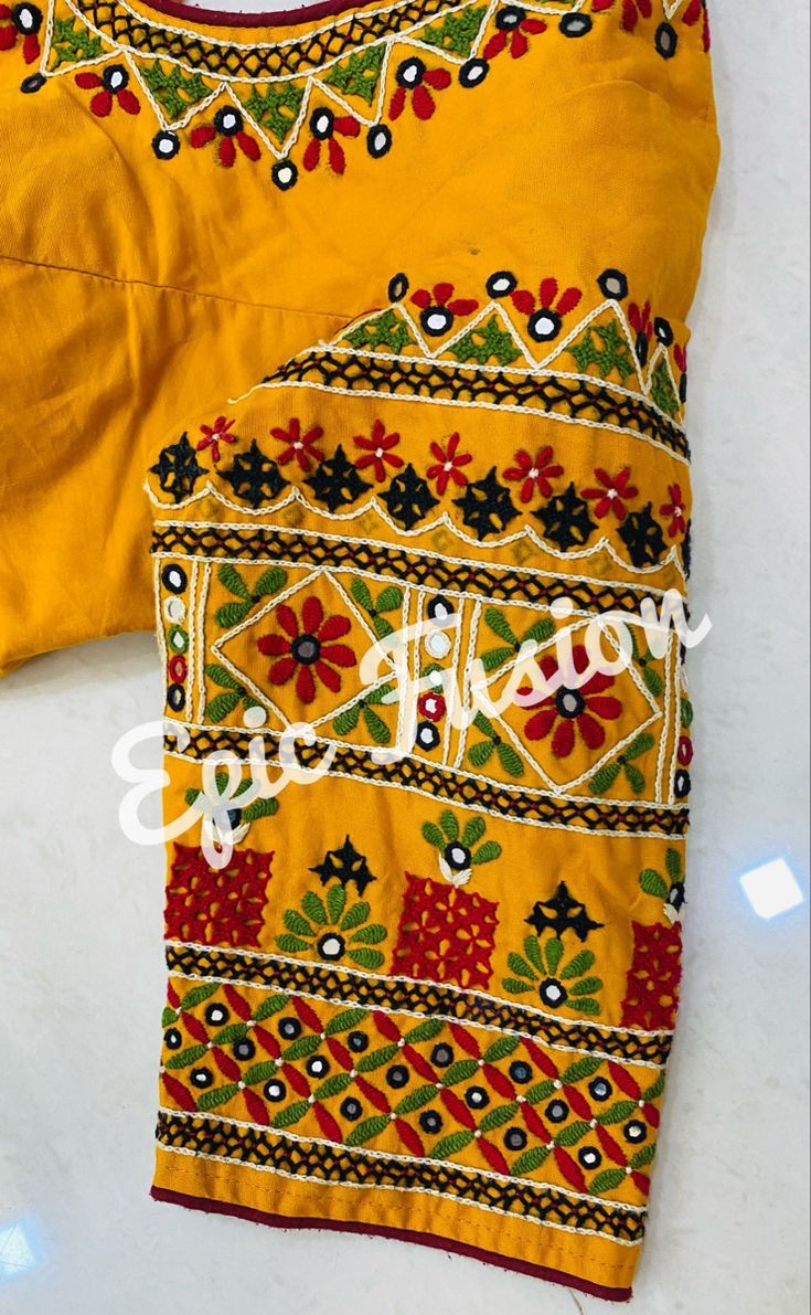 an embroidered yellow shirt with red, green and blue flowers on the chest is laying on a white surface