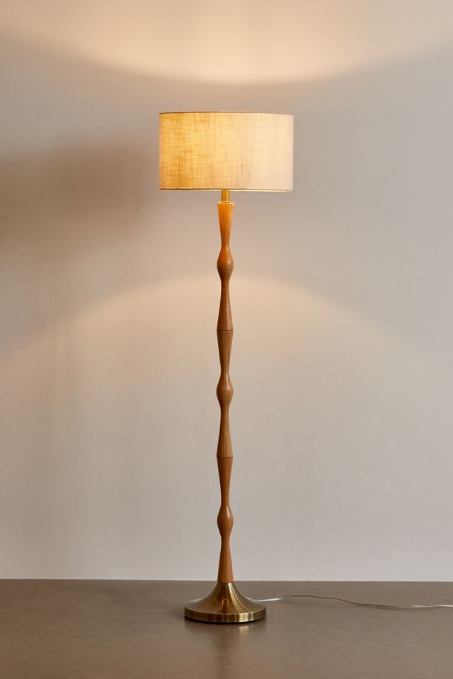 a wooden floor lamp with a white shade on the base and a beige fabric lampshade