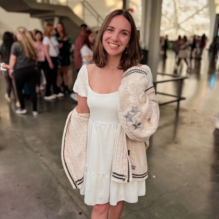 a woman in a white dress and cardigan smiles at the camera