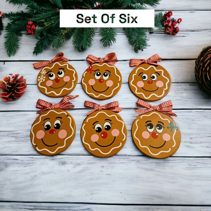 six ginger cookies with faces and bows on them sitting next to pine cones, christmas decorations