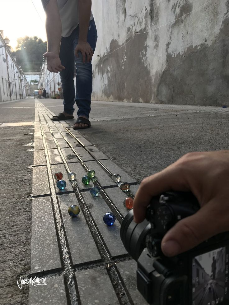 a person holding a camera near small glass balls on the ground and another person standing next to them