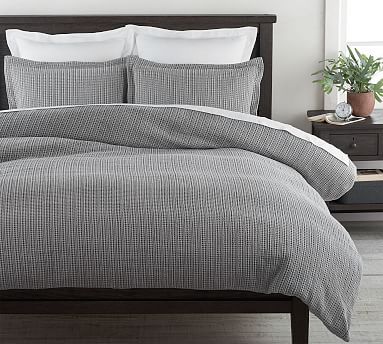 a bed with grey and white comforter in a bedroom next to a plant on a nightstand