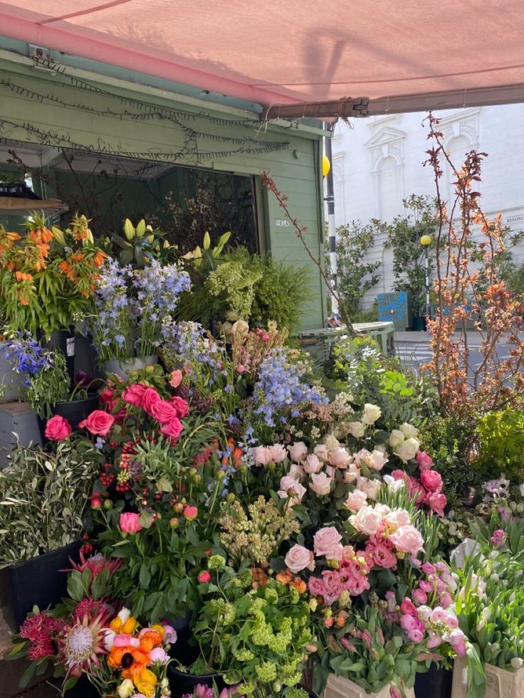many different types of flowers on display under a pink awning in front of a building