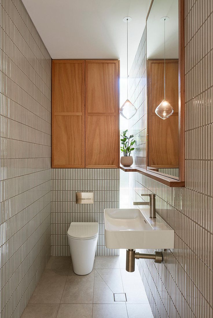 a white toilet sitting next to a sink in a bathroom under a mirror and wooden cabinets