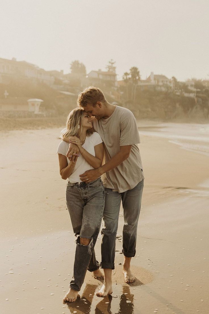 a man and woman walking on the beach with their arms around each other as they kiss