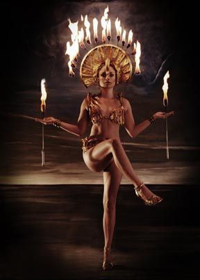 a woman is holding torches in her hands and wearing an elaborate headpiece with flames coming out of it