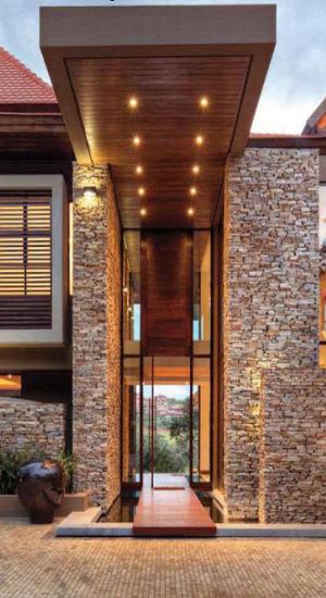 the entrance to a modern house with stone walls and wooden doors, surrounded by brick walkways