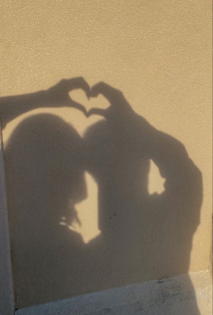 the shadow of a man and woman making a heart shape with their hands on top of each other