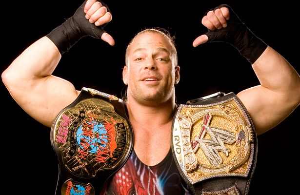 the man is posing with his hands on his head and two wrestling belts around his shoulders
